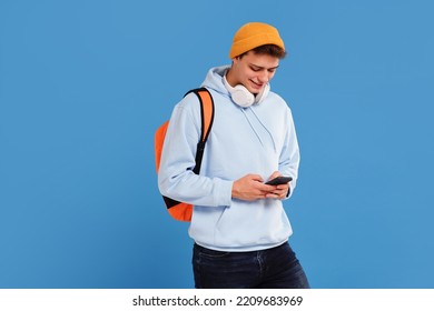 Young fashionable student guy with cap and backpack smiling, using mobile phone, isolated over blue studio background. A lot of copy space.
 - Powered by Shutterstock