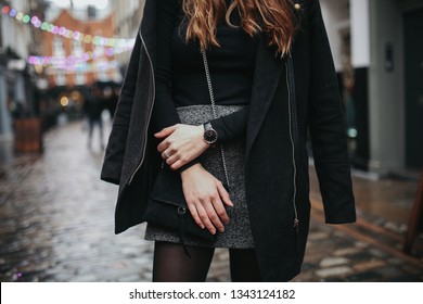 A young fashionable woman under rain wearing black top, black coat and grey skirt. Concept of street style, blogging and lifestyle. Horizontal image with selective focus on the details of the outfit.