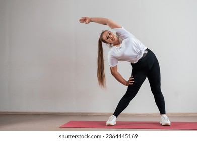 Young fat woman doing flexibility exercises on a white background - Shutterstock ID 2364445169