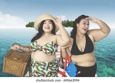 Young Fat Women Looking Something On The Bridge While Carrying Picnic Basket And Beach Items 