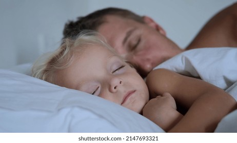 A young father, along with his daughter of two years, sleep soundly next to each other in bed on white bedding. They have deep dreams. They sleep in a bright cozy room. Father guards baby's sleep - Powered by Shutterstock