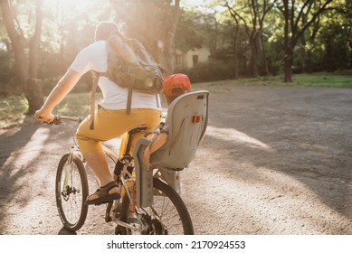 A young father carries his little son in a bicycle seat. dad and son ride a bike. Child safety concept