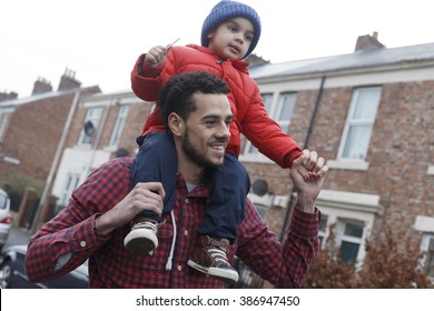 Young father carrying his son on his shoulders as he walks down the street