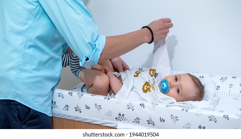 Young Father Changing His Baby Boy's Shirt And Nappy On The Changing Table At Home. Parenting 101.