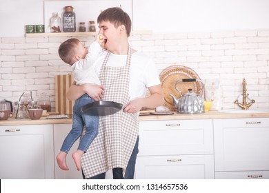 Young Father Cooking With His Little Son. Dad And Child On The Kitchen. Mothers Day Helpers. Man With Kid Making A Dinner Or Breakfast For The Mother.