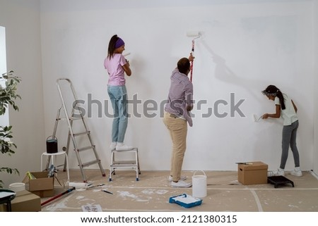 A young father and daughters renovate an apartment in the absence of his wife, surprise, they hold rollers with white paint and precisely painting the walls, a girl climbs a ladder