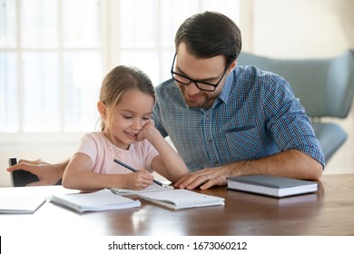 Young father in eyeglasses pleased to see little daughters' study success. Excited smiling small child girl enjoying learning with pleasant dad at home. Children education, home schooling concept. - Shutterstock ID 1673060212