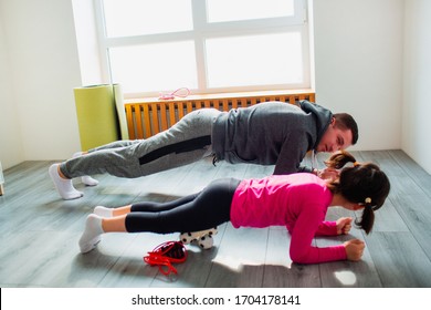 Young Father And His Cute Little Daughter Are Doing Plank On The Floor At Home. Family Fitness Workout. Cute Kid And Daddy Is Training On A Mat Indoor And Have Exercises Near The Window In Room.