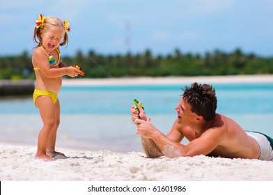 young father and his cute little daughter playing with water guns on exotic beach