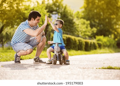 Young father with his little son on motorbike in green sunny park