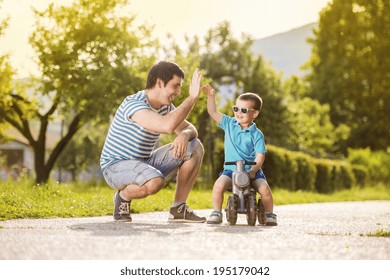 Padre joven con su hijo pequeño en moto en un parque verde y soleado