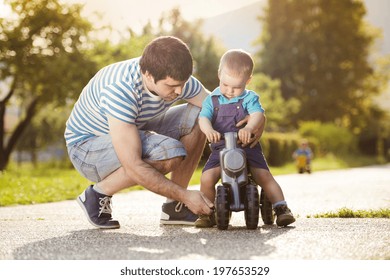 Young father with his little son on motorbike in green sunny park