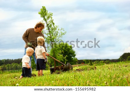 a young father and his two children are outside planting a Dawn Redwood Tree in their yard
