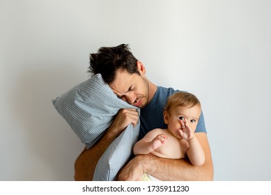 Young father holding his baby in one hand and a pillow in other hand looking tired, trying to sleep. - Shutterstock ID 1735911230
