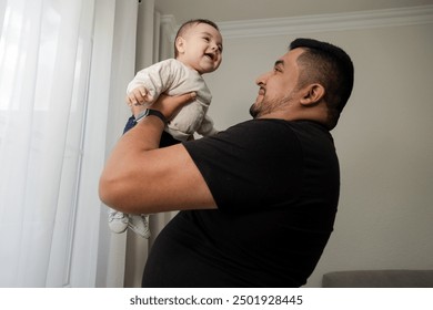 Young father holding his baby smiling in the living room of his house - happy hispanic father with his son - father and son time - fatherhood - Powered by Shutterstock