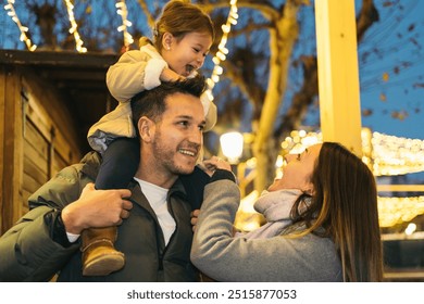 Young father holding his young smiling daughter sitting on his shoulders next to her mother as they visit a city decorated for Christmas. Concept of happy two-parent heterosexual family. - Powered by Shutterstock