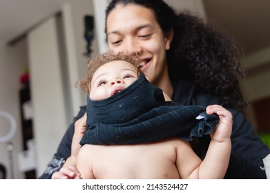 Young Father At Home Helps His Daughter With The Clothes, He Is Putting A Sweater On Her And It Got Stuck On Her Head.