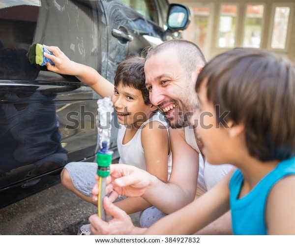 Young\
father and little boys washing car in summer\
day