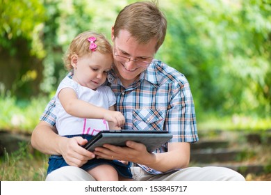 Young father and little  cute daughter reading in summer park