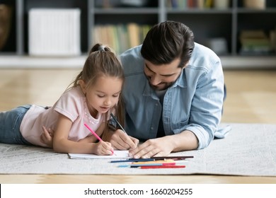 Young father lying on wooden floor with little preschooler daughter drawing together, caring dad have fun relax with small girl child paint in album, family hobby activity, early development concept - Powered by Shutterstock