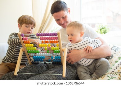 A young father on maternity leave home is teaching his eldest child. The boy learns to count on color beautiful accounts. The younger son sits in the arms of the parent - Powered by Shutterstock