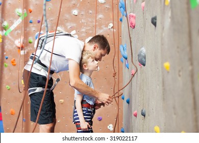 young father preparing his little son for climbing in indoor gym - Powered by Shutterstock