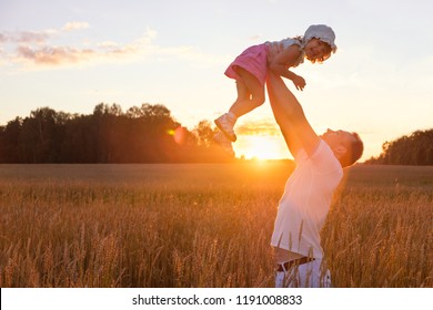 A young father raises his daughter over his head against the background of a wheat field in the setting sun - Shutterstock ID 1191008833