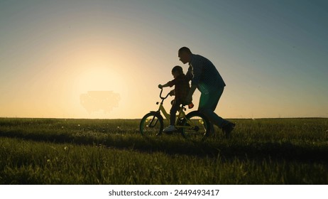 Young father teaches child to keep balance while sitting on bicycle. Childhood dream to ride bike. Dad teaches her little daughter to ride bicycle, sunset. Holiday family. Dad baby, Parental support. - Powered by Shutterstock