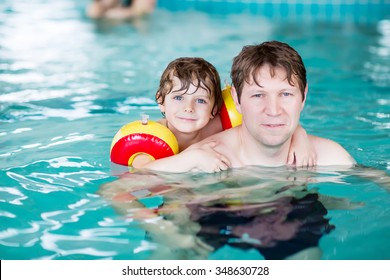 Young Father Teaching His Little Son To Swim In An Indoor Swimming Pool. Active Happy Kid Boy Wearing Safe Swimmies. Family Time.