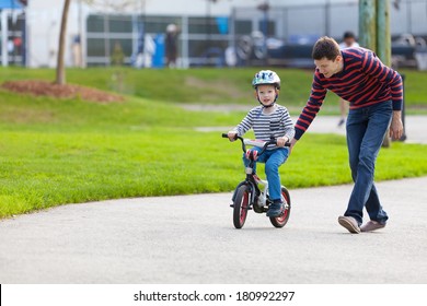 Young Father Teaching His Smiling Son How To Ride A Bike