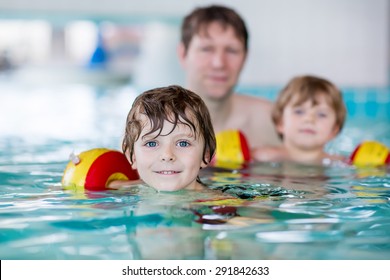 Young Father Teaching His Two Little Sons To Swim In An Indoor Swimming Pool. Active Happy Kid Boys, Siblings And Twins Wearing Safe Swimmies And Having Fun Together.