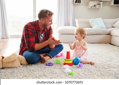 Young Father And Toddler Daughter Clapping In Sitting Room