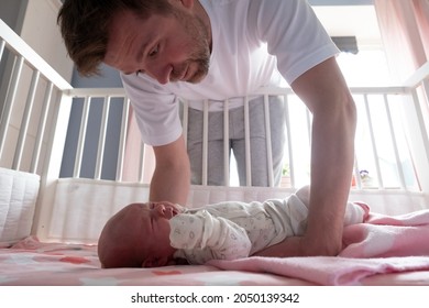 Young Father Trying To Calm Down His Newborn Baby Holding Her In His Hands.