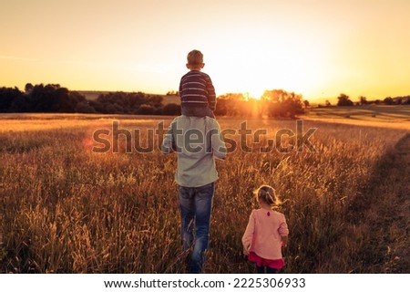Young father walking with his son, daughter children in a country setting watching the beautiful sunset. 