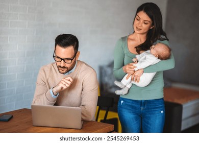 Young father works on laptop while his wife looks after an infant child. Work from home - Powered by Shutterstock