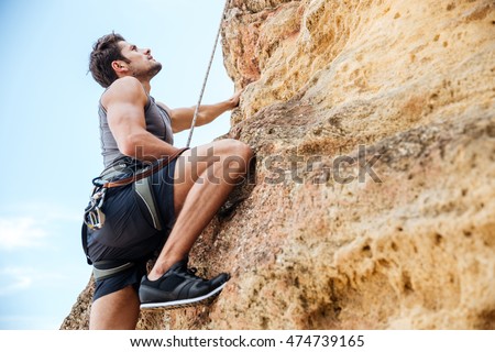 Young fearless man climbing a steep wall in mountain