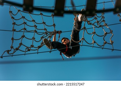 Young Fearless Man Going Through The Net Wall With Ease In The Adventure Park