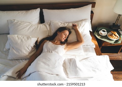 Young female 20 years old in comfy bedclothes watching sweet dreams enjoying sunday morning for long napping in hotel, Caucasian woman lying in cozy bedroom sleeping during lazy day on weekend