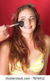 Young Female Adult Fashion Model With Natural Red Hair And Freckles In A Yellow Bikini Getting Make-up (textured Red Faux Leather Background)