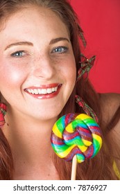 Young Female Adult Fashion Model With Natural Red Hair And Freckles In A Yellow Bikini With A Big Multi-colored Lollipop (textured Red Faux Leather Background)