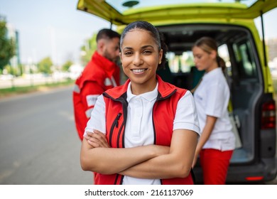 Young female african american paramedic smiling, standing rear of the ambulance, arms crossed. Three paramedics by the ambulance - Powered by Shutterstock