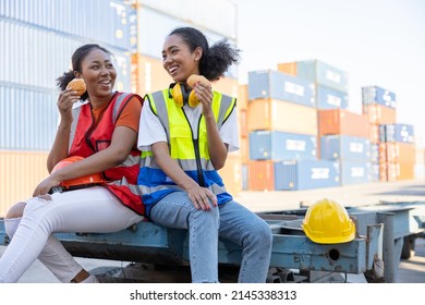 young female African factory workers or engineer having lunch and eating bread together in container warehouse storage