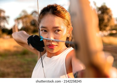 young female archer, archery, shoot arow with bow in nature field to target, success concept, at field for sport exercise at sunset time