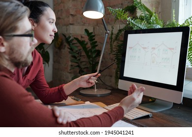 Young Female Architect And Her Male Colleague Discussing New Project In Front Of Computer While Woman Pointing At Sketch Of House On Screen