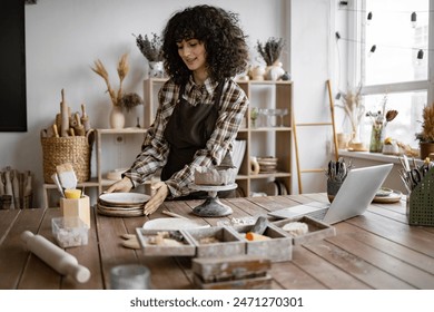 Young female artist organizing tools and materials in pottery studio, focusing on creative work and craftsmanship. - Powered by Shutterstock