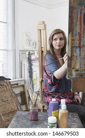 Young Female Artist Painting At Easel In Art Studio