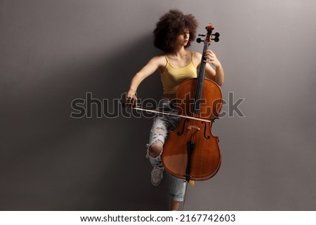 Young female artist playing a cello isolated on gray background