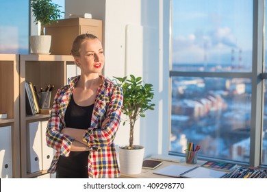 Young female artist standing at art studio, holding arms folded across, her workplace, smiling, looking aside. Designer with artistic tools on work-table ready to work in office. - Shutterstock ID 409298770