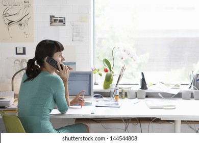 Young female artist using cell phone at desk
