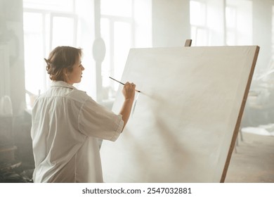 A young female artist working with acrylics on a canvas in a sunlit art studio. - Powered by Shutterstock